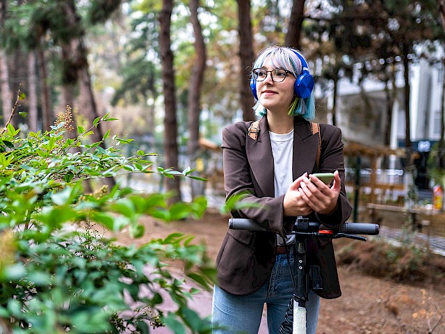 Woman stands on the outskirts and listens to music with headphones.