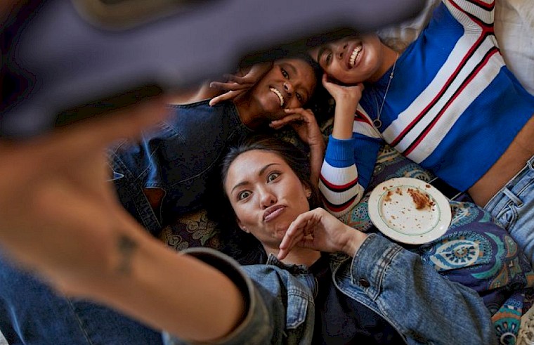 Freundinnen liegen auf dem Boden und nehmen zusammen ein Selfie auf.