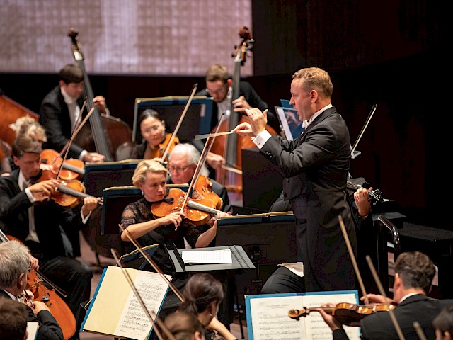 Orchester mit Streichinstrumenten macht Musik auf einer Bühne.